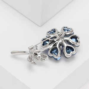 Macro detail of silver flower brooch with blue heart crystals and micro-paved leaves