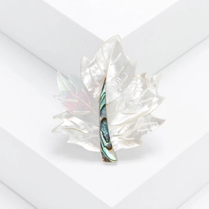 Elegant maple leaf brooch with mother of pearl and abalone inlay on a minimalist white block