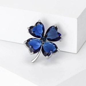 Macro detail of dark blue crystal clover brooch with silver claw setting on white blocks