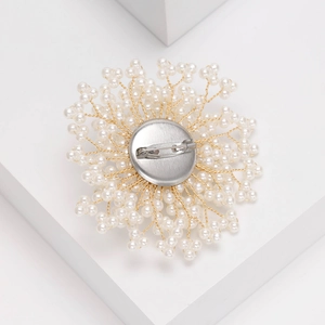 Broche élégante en perles avec fil doré et fermoir de sécurité sur fond blanc