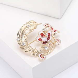 Vue détaillée d'une broche plume et fleur dorée avec émail et strass brillants sur support