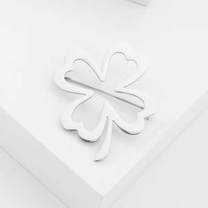 Minimalist silver stainless steel four-leaf clover brooch on a white geometric stand