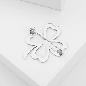 Detail view of silver four-leaf clover brooch with hollow heart petals on white background