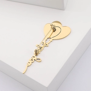Detail of a golden stainless steel heart balloon brooch with cursive love lettering