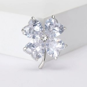 Macro shot of silver four-leaf clover brooch with heart-cut crystals on white podium