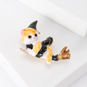 Detail of a white and yellow cat brooch with a black wizard hat riding a golden broomstick