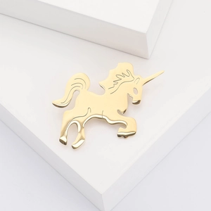 Polished gold unicorn brooch on white geometric stairs, minimalist stainless steel jewelry