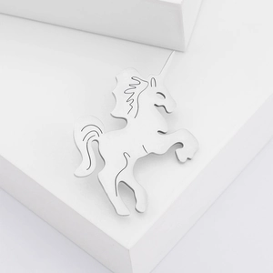 Detail of silver unicorn metal pin with hollow design on white geometric block