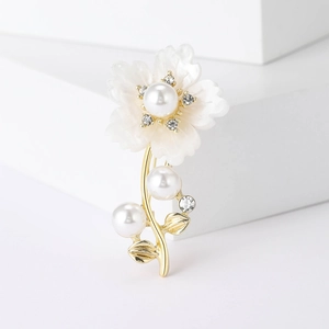 Gros plan d'une broche fleur élégante avec base dorée, perles blanches et cristaux
