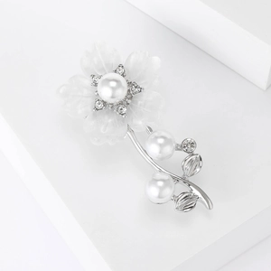 Gros plan sur une broche fleur élégante avec pétales blancs, perle et strass brillants