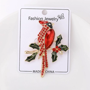 Détail d'une broche oiseau cardinal rouge avec strass brillants et feuilles en émail vert