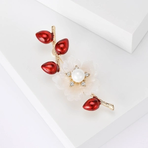 Detail einer eleganten Blumenbrosche mit weißer Blüte, roten Knospen und zentraler Perle