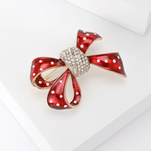 Détail d'une broche noeud en émail rouge à pois blancs et centre en strass brillant