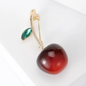Elegante spilla a ciliegia con frutto rosso traslucido e foglia verde su base bianca