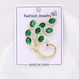 Vue détaillée d'une broche paon en cristal avec gemmes vert émeraude et dorure