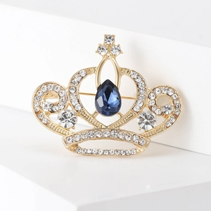 Détail d'une broche couronne dorée avec cristal bleu poire et strass blancs scintillants