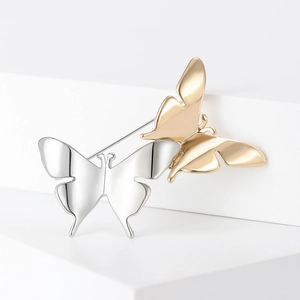 Spille a farfalla minimaliste oro e argento con finitura lucida su piedistallo bianco