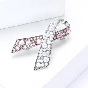Détail d'une broche ruban argentée avec perles blanches et strass roses sur socle blanc