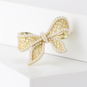 Elegant gold bow brooch with white pearls and quilted texture on geometric cubes