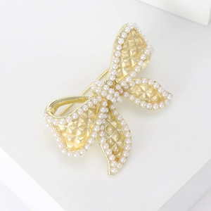 Detail of golden bow brooch with elegant quilted pattern and white pearl trim embellishment