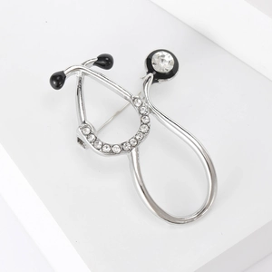 Macro shot of silver stethoscope brooch featuring sparkling rhinestones and black enamel