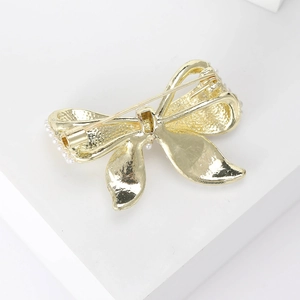 Elegant gold bow brooch with pearl edges shown from a high-angle close-up view