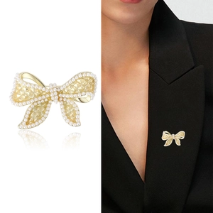 Elegant gold bow brooch with pearls and quilted texture shown on a blazer lapel