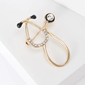 Detailed view of a gold-plated stethoscope brooch with sparkling white crystals