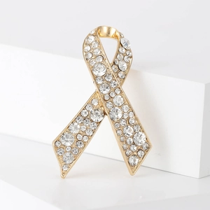 Élégante broche en forme de ruban doré ornée de strass brillants sur fond blanc épuré