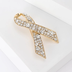 Vue détaillée d'une broche ruban dorée sertie de strass brillants sur des blocs blancs