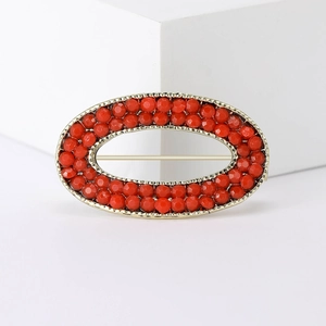 Macro detail of oval gold brooch featuring red beaded edges and secure pin backing