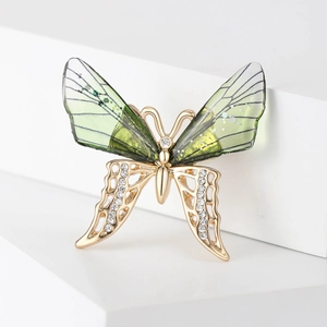 Detail view of a golden butterfly brooch with emerald green wings and sparkling rhinestones
