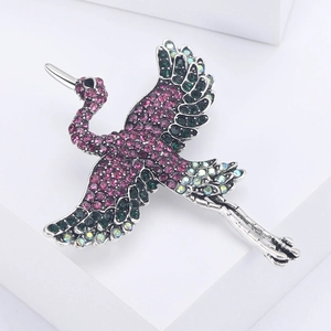 Macro shot of silver crane brooch with pink and green rhinestones on white stand