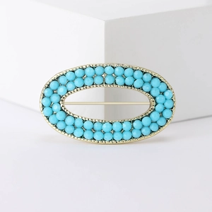 Vintage gold oval brooch with turquoise blue beads on a minimalist white display