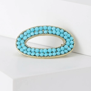 Vintage oval gold-toned alloy brooch with light blue beads on white geometric platform