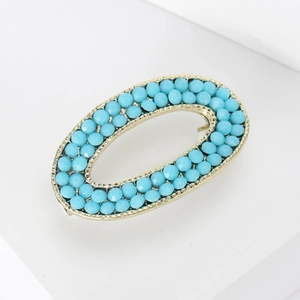 Detailed macro view of an oval gold brooch with turquoise blue beads on a white podium