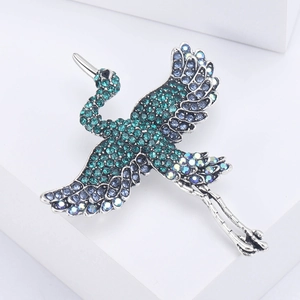 Elegant silver crane brooch with sparkling blue and green crystals on a white pedestal