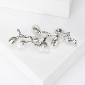 Back view of silver peach branch pearl brooch showing safety pin clasp on a stone block
