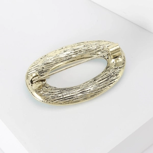 Golden oval geometric brooch with textured bark finish on a minimalist white stand