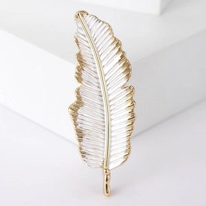 Close-up of elegant gold-edged feather brooch with silver texture on white display