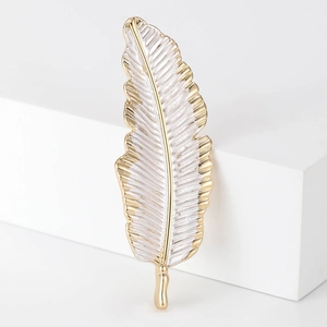 Detailed close-up of golden feather brooch with white enamel texture on elegant stand