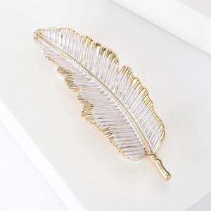 Detail of elegant gold-rimmed feather brooch with white enamel texture on white pedestal