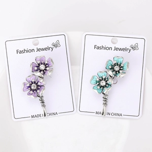 Close-up of enamel flower brooches with purple and teal petals and crystal accents