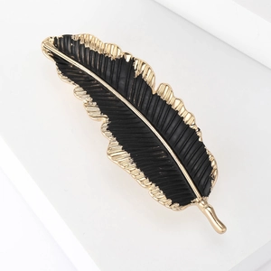 Elegant feather brooch in black and gold finish on a minimalist white platform