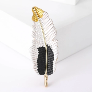 Detailed view of an elegant feather-shaped brooch in gold, black and white enamel finish