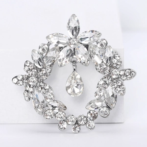 Macro detail of silver crystal wreath brooch with sparkling teardrop pendant on white base