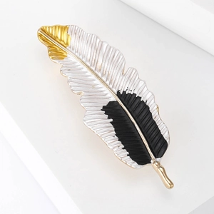 Elegant silver feather brooch with gold accents and black texture on white stand