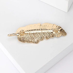 Elegant gold leaf feather brooch with polished alloy texture on a minimalist white pedestal