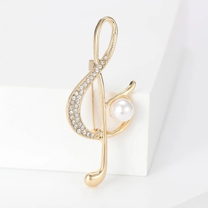 Elegante spilla a nota musicale dorata con strass e perla bianca su supporto bianco