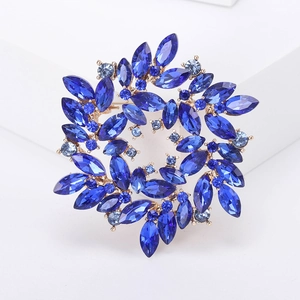 Detailed close-up of golden brooch with deep blue rhinestones on white geometric props